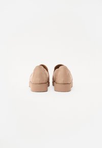 Pantofi slip-on din sueded bej, cu vârf rotund, talpă plată din cauciuc și detalii minime de coasere, văzuți din spate.