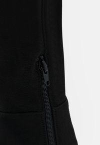Gros plan sur un vêtement en polaire noire avec une fermeture éclair noire partiellement fermée sur une couture verticale.