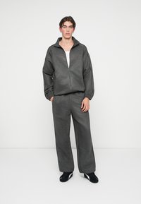 Halli halliga tõmblukuga jakke ja sobivad hallid püksid. Kanga välimus on pehme, veidi tekstureeritud. Komplekti lõpetavad mustad jalanõud.