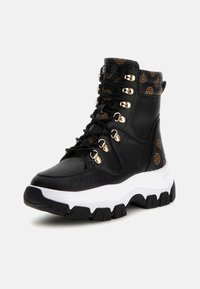 Bottines noires avec quincaillerie dorée, en cuir texturé, détail de logo, épaisse semelle blanche, et un accent noir et marron à motifs sur la tige.