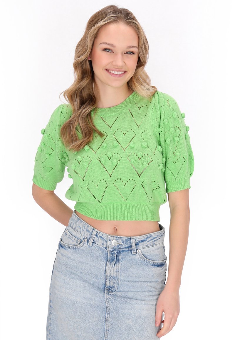 Suéter de punto verde cortito con patrones de corazones y bobbles texturizados, mangas cortas y un escote redondo, combinado con una falda de mezclilla clara.