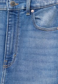 Jean en denim avec un lavage bleu clair, design classique à cinq poches, surpiqûres contrastantes et détails en métal.