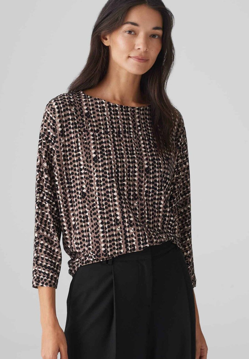 Langärmliges Oberteil aus strukturiertem Stoff mit einem geometrischen Punktmuster in Schwarz- und Beigetönen, mit einer lockeren, drapierten Passform.