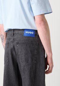 Fadede sorte jeans med en struktureret finish, der har en blå læderlap med "HUGO" branding på bagsiden, samt almindelige lommer.