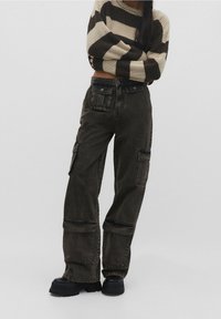 Cargo pants in dark wash denim, featuring side pockets, a relaxed fit, and contrasting stitching. Paired with a striped knit sweater.