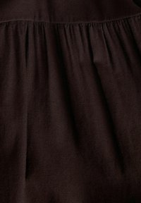 Σκούρο καφέ ύφασμα με πτυχές που δημιουργούν κάθετες πτυχώσεις και υφή, παρουσιάζοντας μια κοντινή εικόνα λεπτομέρειας κλωστοϋφαντουργίας.