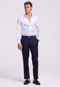 Wit overhemd met lange mouwen, marineblauwe broek, zwarte riem en zwarte instappers; gladde stof met een button-down kraag en een getailleerde pasvorm.