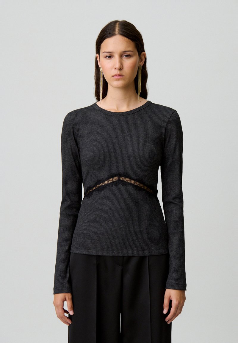 Top nero a maniche lunghe in costina con inserti in pizzo in vita. Presenta un collo rotondo e una silhouette aderente. Tessuto morbido.