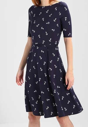 Robe bleu marine longueur genoux avec manches courtes, taille cintrée et motifs d'ancre blancs portée par une personne sur un fond uni.