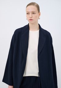 Navy textured kimono jacket with a shawl collar over a cream crew neck shirt. Soft fabric with wide sleeves, relaxed fit, and minimal design.