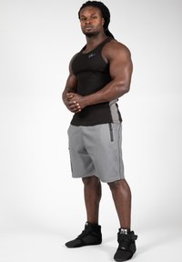 Zwarte mouwloze tanktop met grijze accenten, gecombineerd met grijze shorts met ritszakken en een gestructureerd patroon. Model draagt zwarte sportschoenen.