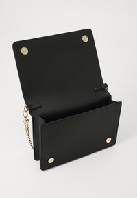 Svart lær clutch med en glatt tekstur, som har en gyllen kjede-rem, magnetisk trykklås og to sirkulære gulldetaljer foran.