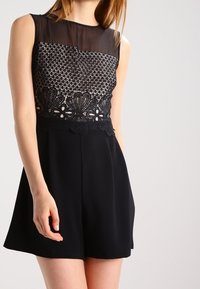 Mono negro con parte superior de malla transparente y detalles de encaje intrincados alrededor de la cintura, con una parte inferior corta y acampanada. Textura suave.