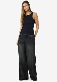 Top negro sin mangas combinado con jeans de pierna ancha de color gris oscuro, holgados. Tejido suave, con un diseño minimalista y una silueta recta.