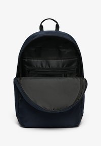 Mochila azul marino con un bolsillo frontal con cremallera, un interior organizado que incluye compartimentos de malla y con cremallera, y un asa de tela en la parte superior.