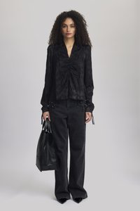 Blusa nera con texture e dettagli arricciati, maniche lunghe e legacci ai polsini, abbinata a jeans neri a vita alta e a una borsa tote nera.