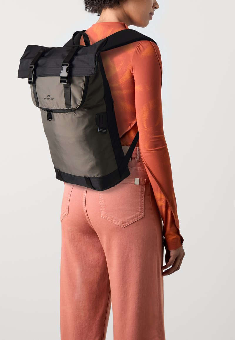 Un sac à dos en matériaux olive et noir, doté d'un rabat repliable et de bretelles ajustables. Le tissu texturé et les couleurs contrastantes améliorent le design.