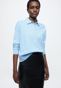 Lichtblauwe gebreide polotrui met een kraag en vijf knopen, gecombineerd met een zwarte leren rok, met een gladde textuur en een nauwsluitende pasvorm.