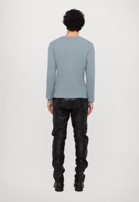 Šviesiai mėlynas ilgarankovė megztinis su įlinkimu, derinamas su juodomis odinėmis kelnėmis, turinčiomis užtrauktukus ant kulkšnies. Siluetas aptakus, apvaliu kaklu.