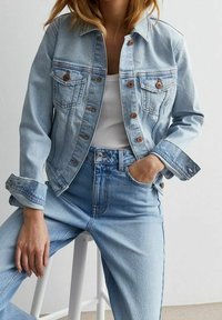 Vaaleansininen farkkutakki, jossa on kaksi rintataskua, napitus ja klassinen kaulus. Yhdistetty vaaleansinisiin korkeavyötäröisiin farkkuihin.