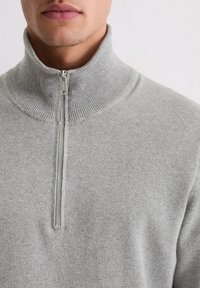 Szary sweter zapinany na zamek z wysokim prążkowanym kołnierzem, wyposażony w srebrny zamek błyskawiczny i teksturowany wzór dzianiny.