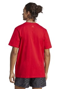T-shirt in cotone rosso con scollo a girocollo e maniche corte. Logo Adidas ricamato in tonalità sulla parte superiore della schiena. Vestibilità rilassata.
