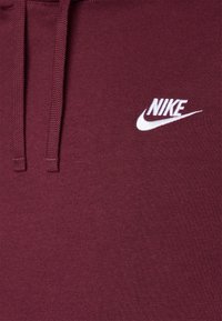 Sudadera burdeos hecha de un tejido suave con un logo blanco de Nike en el pecho y cordones para la capucha. Diseño simple y elegante.