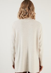 Cremfarbener Pullover mit langen Ärmeln, gerippter Textur und seitlichen Schlitzen; hat eine lockere Passform und einen runden Halsausschnitt.