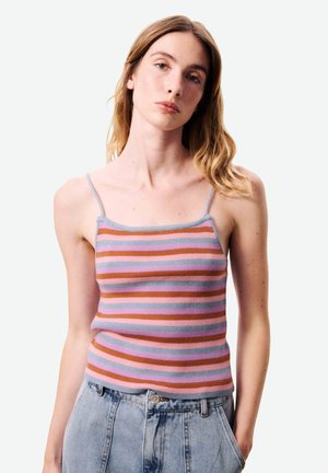 Jeune femme aux cheveux châtain clair portant un débardeur sans manches à rayures multicolores et un jean taille haute bleu clair.