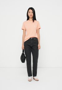Coral t-shirt with short sleeves, black high-waisted jeans, light pink flats, and a small black bag. Simple, casual outfit.