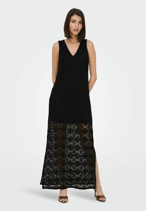 Woman wearing a sleeveless black lace maxi dress with a V-neck and side slit, paired with brown open-toe heeled sandals.