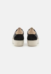 Sneaker neri e beige realizzati in suede e materiale tessile, forma arrotondata, suola piatta in gomma e dettagli in metallo dorato sul tallone.