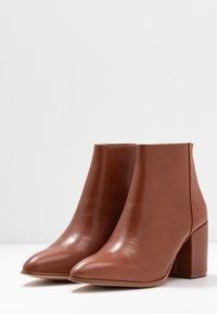 Bottes chevilles en cuir marron avec un bout pointu, un talon bloc et une texture lisse. Design minimaliste sans ornements supplémentaires.