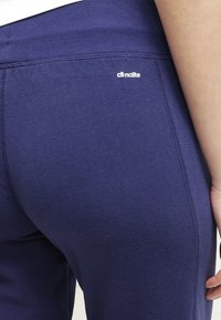 Tummansiniset urheilulegginsit, jotka on valmistettu pehmeästä kankaasta ja joissa on korkea vyötärö. Takana on pieni valkoinen "climalite"-logo.