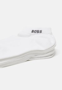 Chaussettes en coton blanc empilées, avec un haut court portant l'inscription "BOSS" en gris sur le bord. Texture douce, couleur unie et design décontracté.