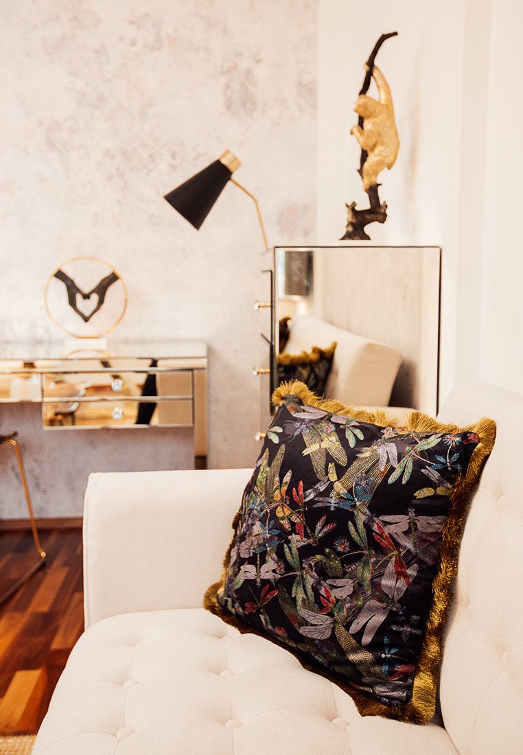 Schwarzes Kissen mit Blumenmuster und mehrfarbiger Stickerei, mit goldenen Fransen, das auf einem cremefarbenen Sofa in einem stilvollen Innenraumruhen.