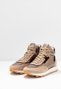 Wysokie trampki wykonane z beżowego zamszu i błyszczącej brązowej skóry, z teksturowanymi akcentami, beżowymi sznurówkami i gumową podeszwą.