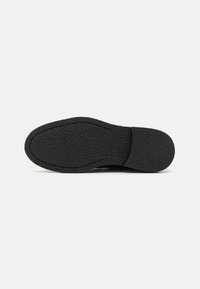 Semelle de chaussure en caoutchouc noir avec une surface texturée, une forme courbée et des coutures visibles le long des bords, conçue pour l'adhérence et la durabilité.