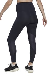 Leggings neri a vita alta con pannelli laterali testurizzati, caratterizzati da una finitura liscia e un design aderente. Indossati con scarpe sportive nere.