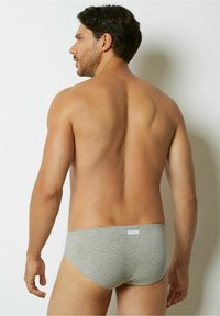 Grå bomullskalsonger med en slät yta, elastiskt midjeband och minimal logodetalj, sett bakifrån mot en neutral bakgrund.