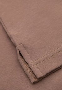 Tejido marrón claro con una textura suave, que presenta un dobladillo de manga doblado y un detalle de costura limpia a lo largo de los bordes.