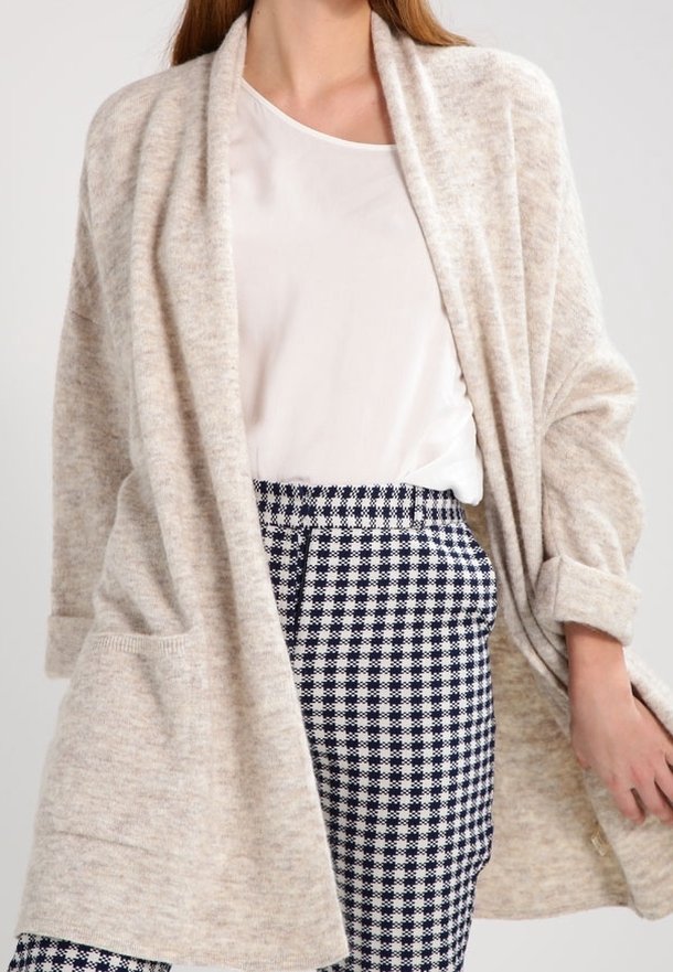 Beige Strickjacke mit offenem Vorderteil, langen Ärmeln und Taschen, kombiniert mit navyblauen und weißen Hahnentrittmuster-Hosen.