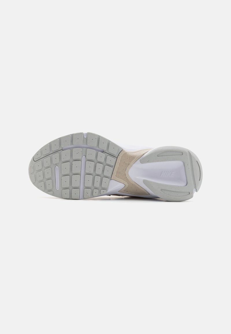 Semelle de chaussure de sport blanche avec une surface en caoutchouc gris texturé, présentant des motifs rectangulaires et un accent beige près du talon.