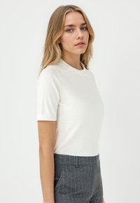 Weißes Kurzarm-Oberteil mit rundem Ausschnitt, glatter Textur und tailliertem Schnitt, kombiniert mit grauen Nadelstreifen-Hosen.