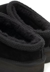 Černá pantofle s měkkým, plyšovým vnitřkem a sametovým vnějškem. Má pletený okraj a gumovou podrážku pro lepší přilnavost.