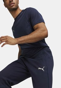 Marinblå atletisk t-shirt och byxor med kontrasterande sömmar och en Puma-logotyp. Tyget ser slätt ut med en avslappnad passform.