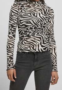 Långärmad, figurnära topp i genomskinligt tyg med ett svartvitt zebramönster. Design med hög krage. I kombination med svarta jeans.