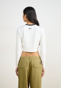 White cropped long-sleeve shirt with black collar, featuring a small black Nike logo on the back. Olive green cargo pants with pockets.