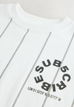 T-shirt blanc avec des rayures horizontales grises, arborant un imprimé circulaire noir comprenant du texte et des coordonnées. Tissu en coton doux.