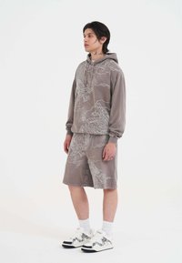 Grauer Kapuzenpullover mit weißen Drachen- und Wolkendesigns, kombiniert mit passenden Shorts. Der Stoff hat eine weiche Textur. Getragen mit weißen Turnschuhen.